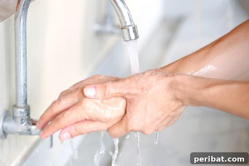 A person washing grimy hands under running water, with a bottle of vinegar in the background for cleaning.