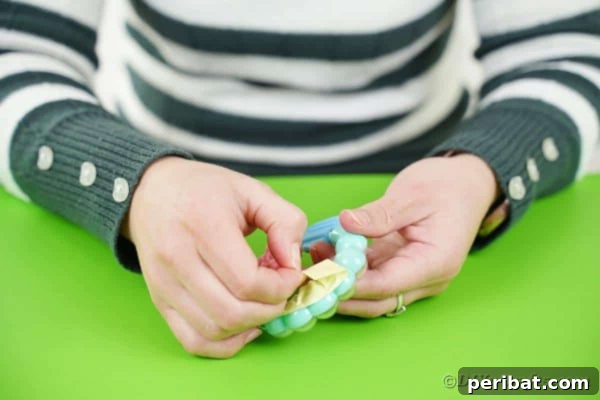 Applying double-sided tape to the back of a baby rattle before attaching it to the guitar neck