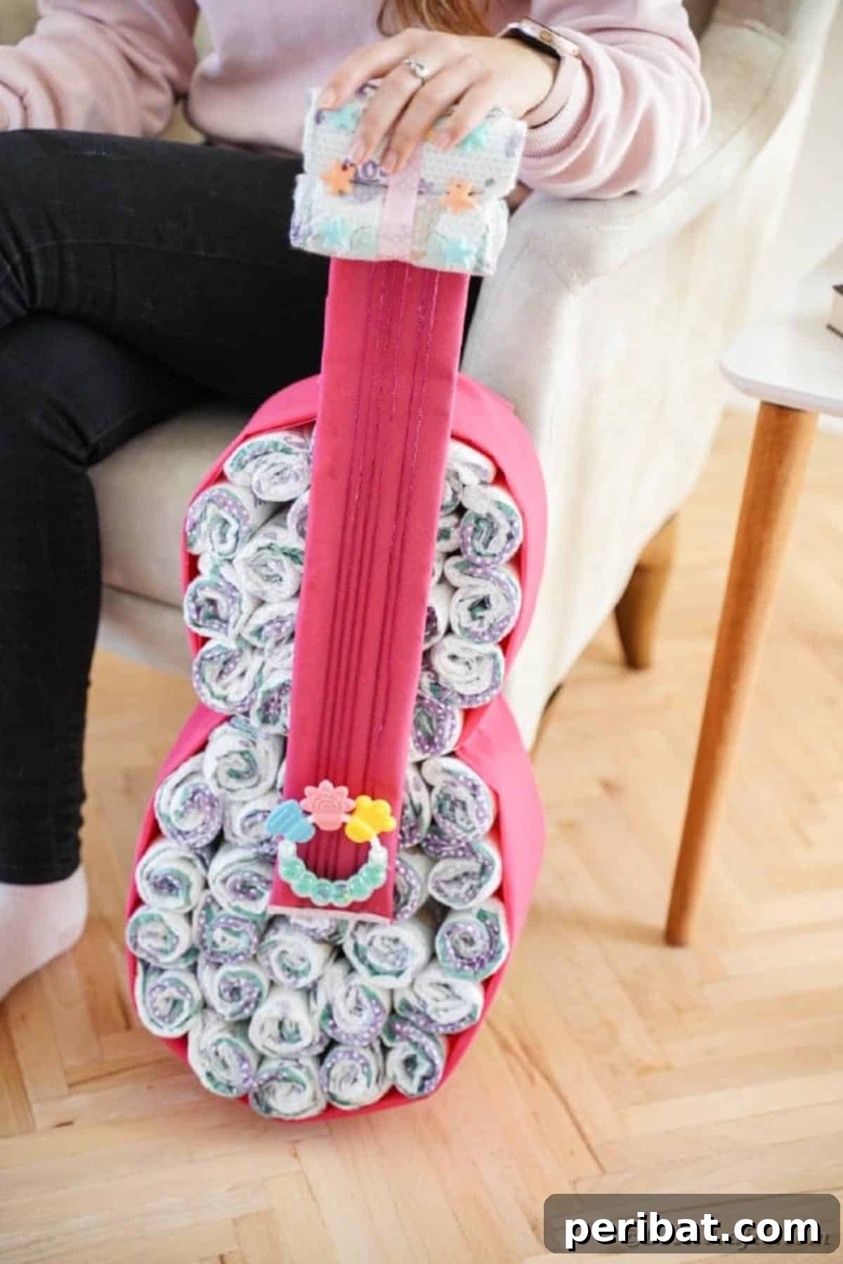 A woman proudly sitting beside the completed guitar diaper cake, showcasing the final, decorated gift