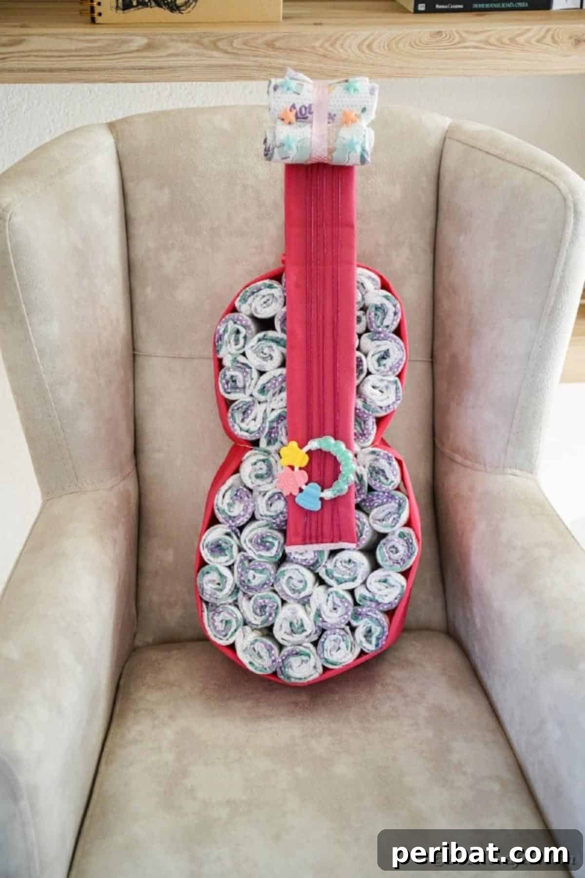 A vibrant guitar diaper cake resting on a tan armchair, demonstrating color customization options
