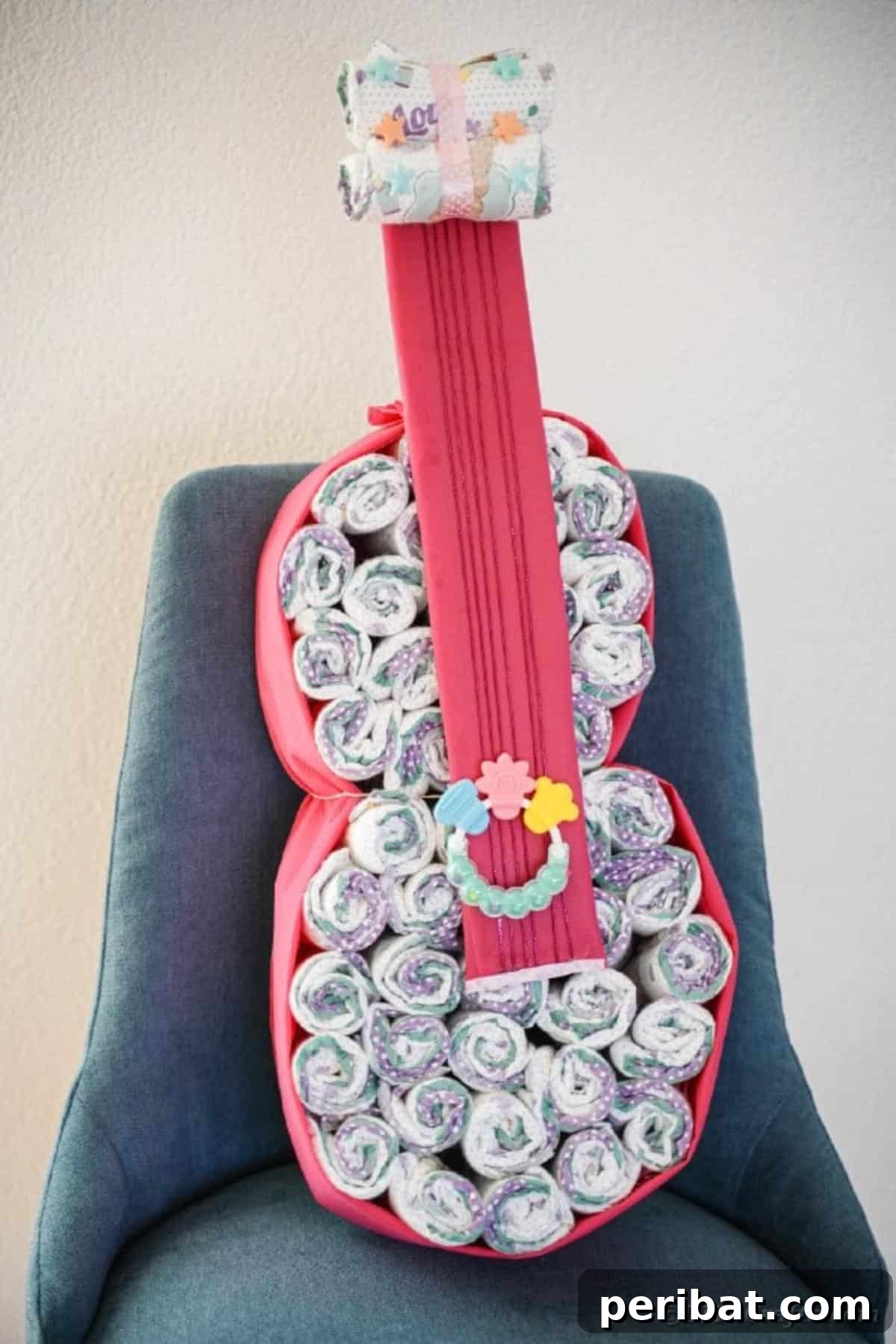 A guitar diaper cake displayed on a bright blue chair, showing how rolled washcloths or blankets can replace some diapers
