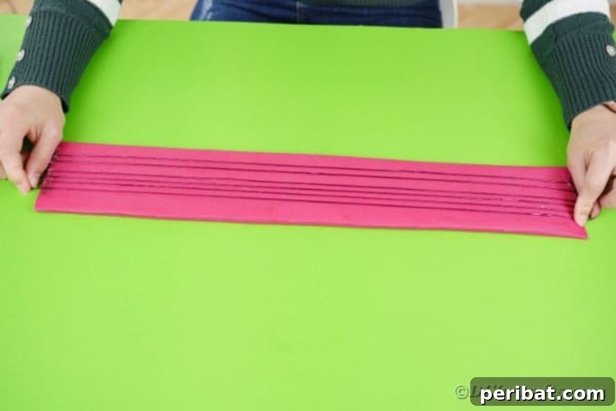 Hands carefully attaching thin strings or ribbons to the covered cardboard neck, mimicking guitar strings