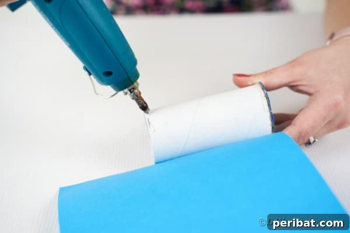 Gluing blue craft paper around the toilet paper roll base
