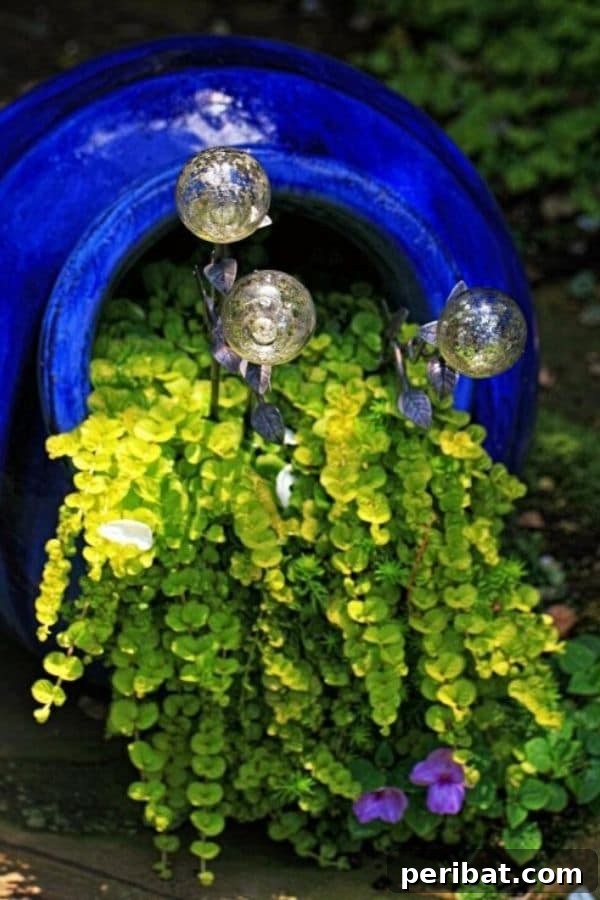 Cascading Flower Pot Art for Stunning Garden Decor 3 Lush green ground cover and sparkling gazing balls flowing from a bright blue pot, evoking a serene, Mediterranean summer feel.