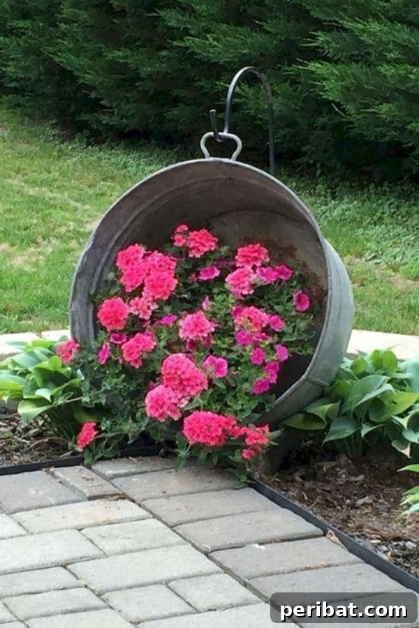 32 DIY Vintage Garden Crafts to Add Rustic Charm 8 A galvanized washtub planter filled with pink flowers, suspended from a shepherd's hook in a garden.