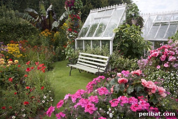 A charming glass greenhouse with white trim nestled within a lush flower garden, combining functionality with aesthetic appeal
