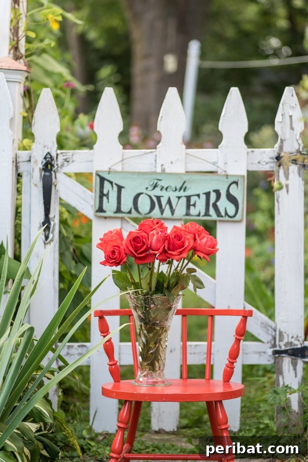 Wooden sign reading 'Fresh Flowers' hanging by a garden gate near a red chair