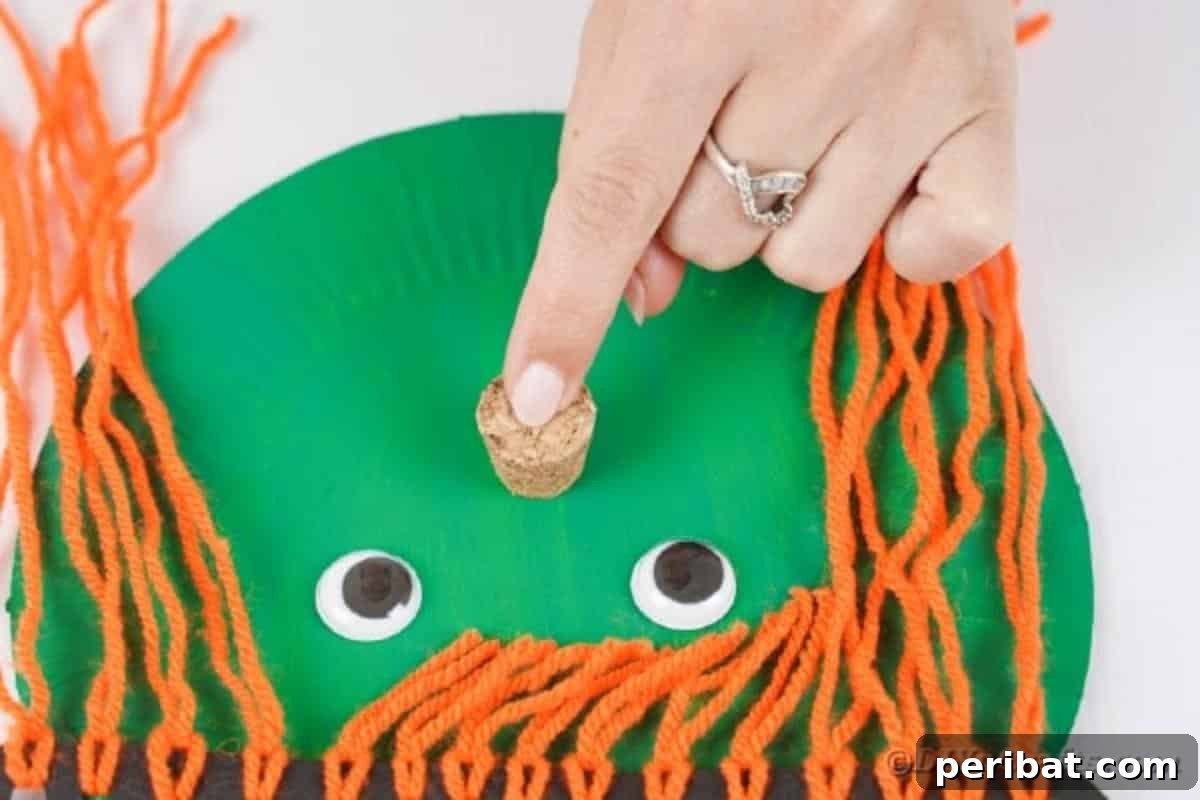 Spooktacular Paper Plate Witch Craft 17 Gluing a cork piece as the nose on the paper plate witch