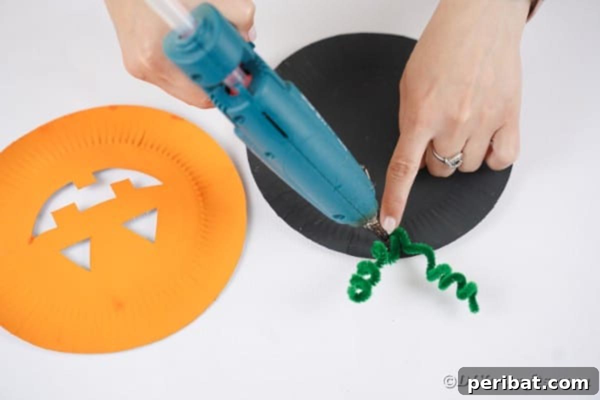 Grinning Gourd Lanterns: A Paper Plate Craft for Kids 13 Gluing the pipe cleaner stem to the top of the black-painted plate