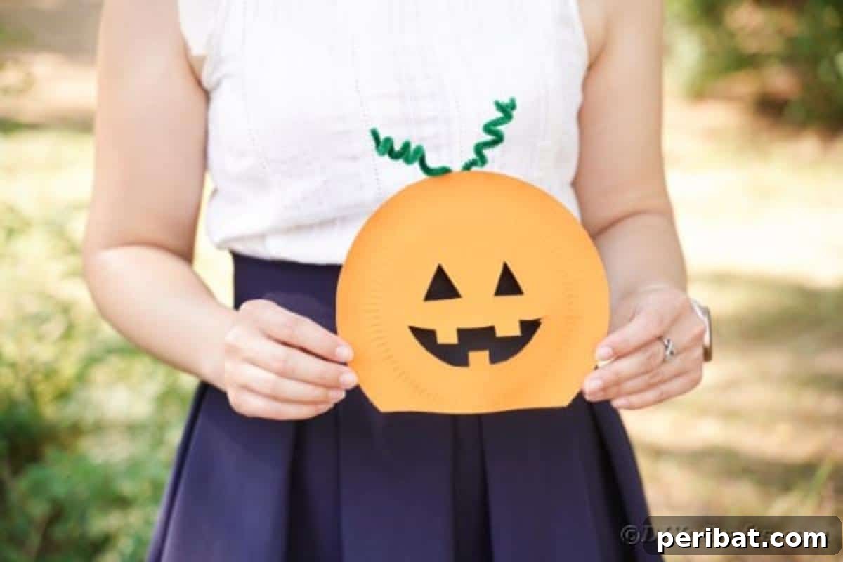 Grinning Gourd Lanterns: A Paper Plate Craft for Kids 5 Woman holding a finished paper plate pumpkin craft