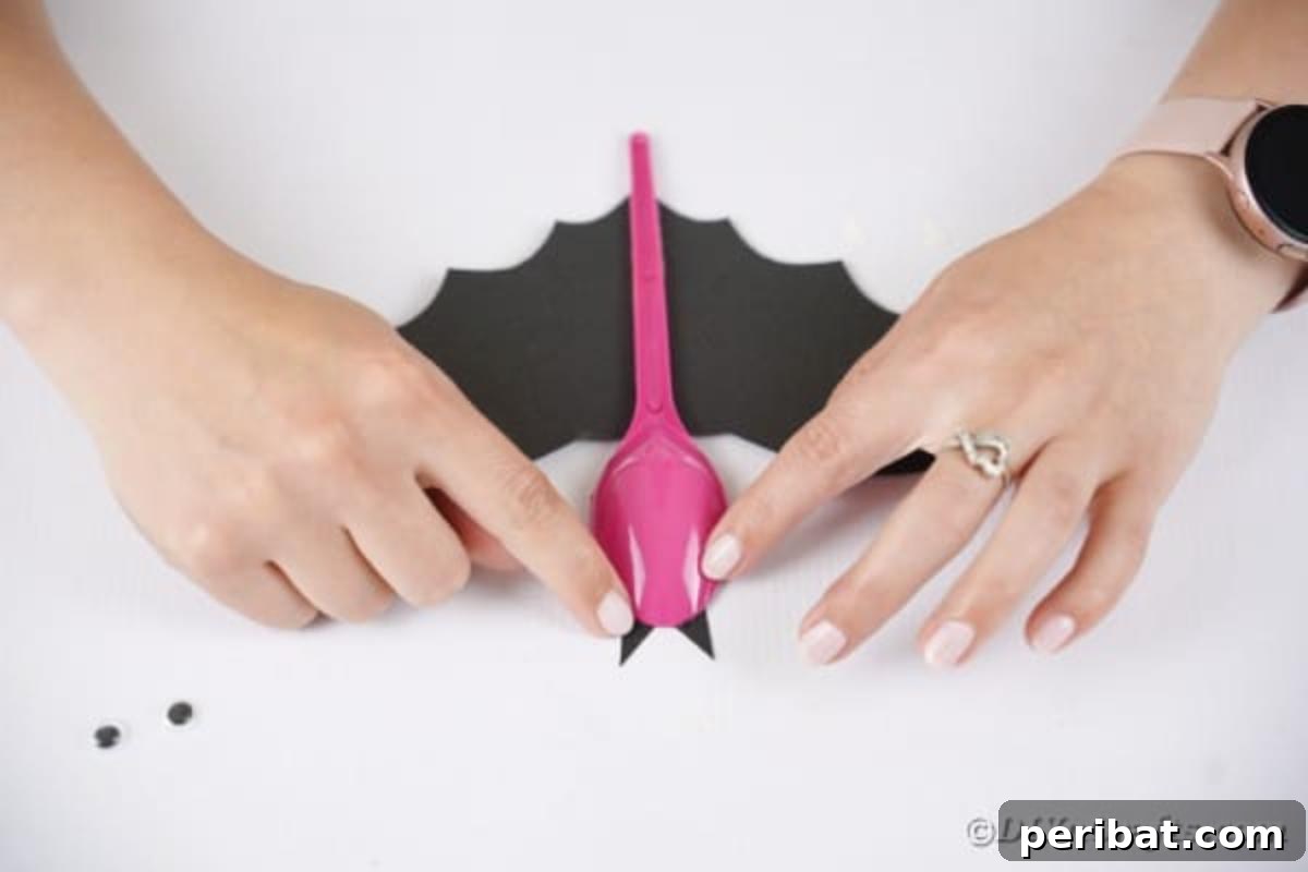 Adorable Recycled Plastic Spoon Bat Halloween Decor 14 A small black paper triangle being glued to the top of the spoon, forming one of the bat's ears, adding character to the upcycled Halloween craft.