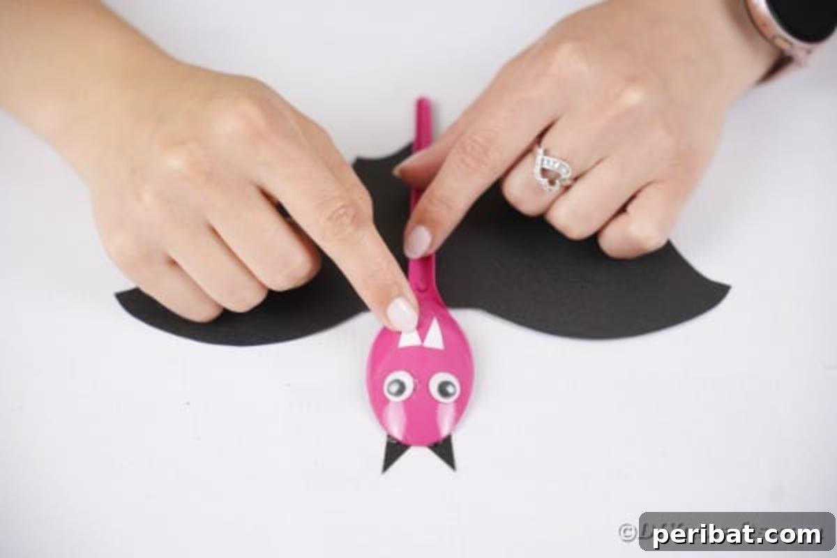 Adorable Recycled Plastic Spoon Bat Halloween Decor 16 Two tiny white paper triangles being glued to the bottom of the spoon's face, forming the bat's cute, slightly spooky teeth.