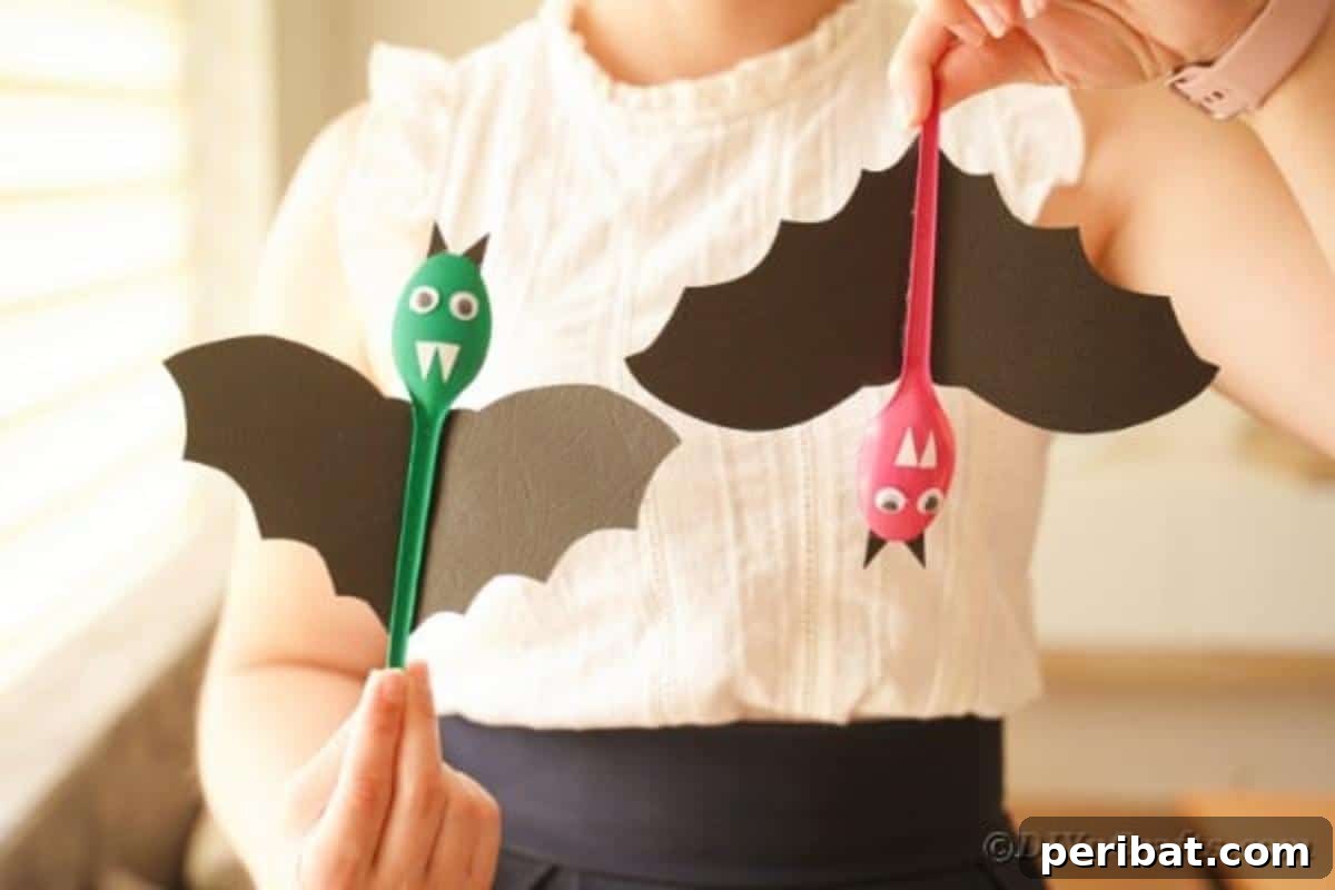Adorable Recycled Plastic Spoon Bat Halloween Decor 3 A person gently holding a finished upcycled spoon bat, showcasing its detailed construction with painted spoon body, paper wings, and googly eyes, ready for Halloween decoration.