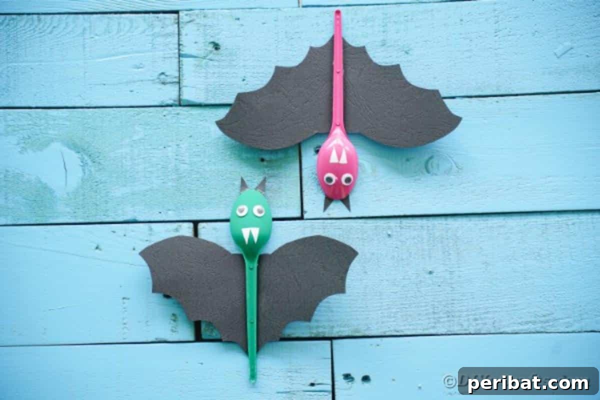 Adorable Recycled Plastic Spoon Bat Halloween Decor 4 A close-up of multiple colorful upcycled spoon bats arranged on a textured blue surface, highlighting their varying paint colors, black paper wings, and cute facial features.