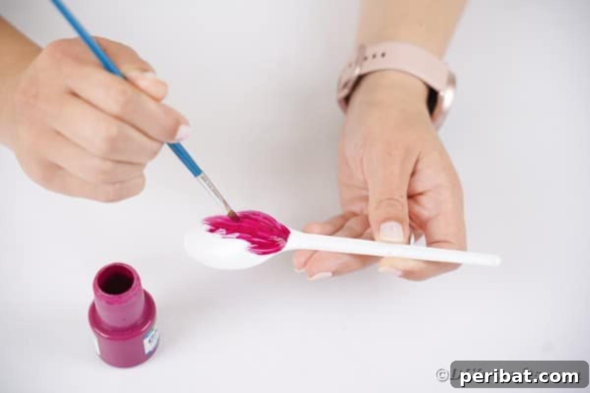 Adorable Recycled Plastic Spoon Bat Halloween Decor 9 A hand painting a plastic spoon vibrant pink, preparing it to be transformed into a charming upcycled Halloween bat decoration.