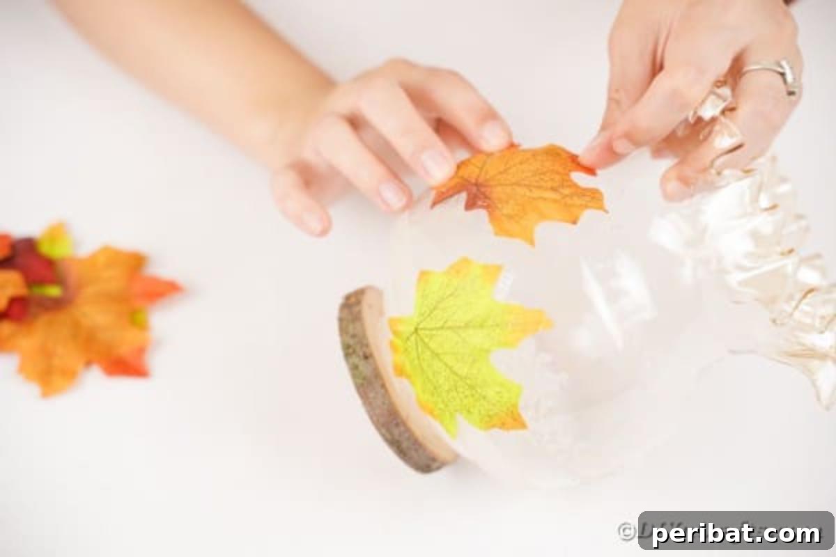 Autumn Leaf Jar Luminaries 11 A hand gently smoothing down an artificial fall leaf glued to a jar, potentially with an extra layer of adhesive, ensuring all edges are secure.