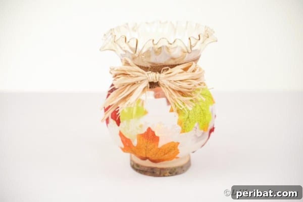 Autumn Leaf Jar Luminaries 15 A raffia bow being glued onto the front of a fall leaf jar, specifically placed over the seam of the burlap ribbon, to complete the rustic decoration.