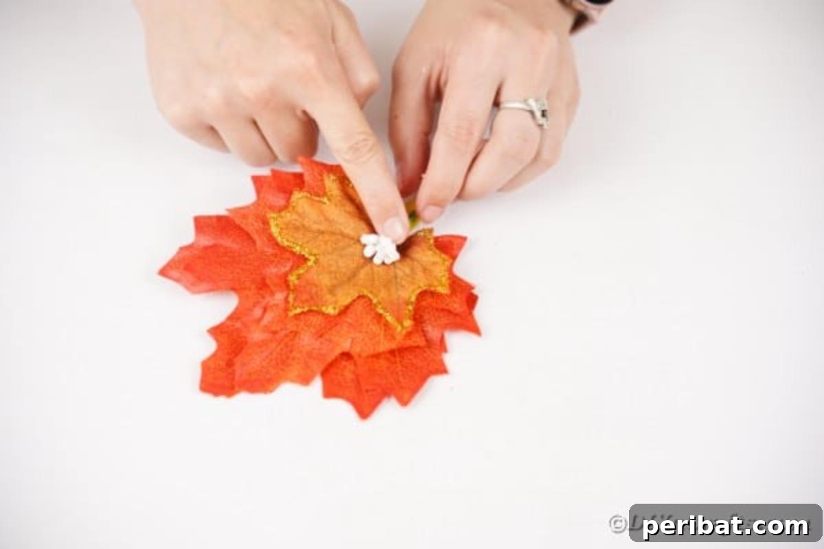 Elegant Autumnal Foliage Wedding Boutonnière 13 A small sprig of artificial flowers being carefully glued onto the stacked fall leaves, adding a delicate accent.
