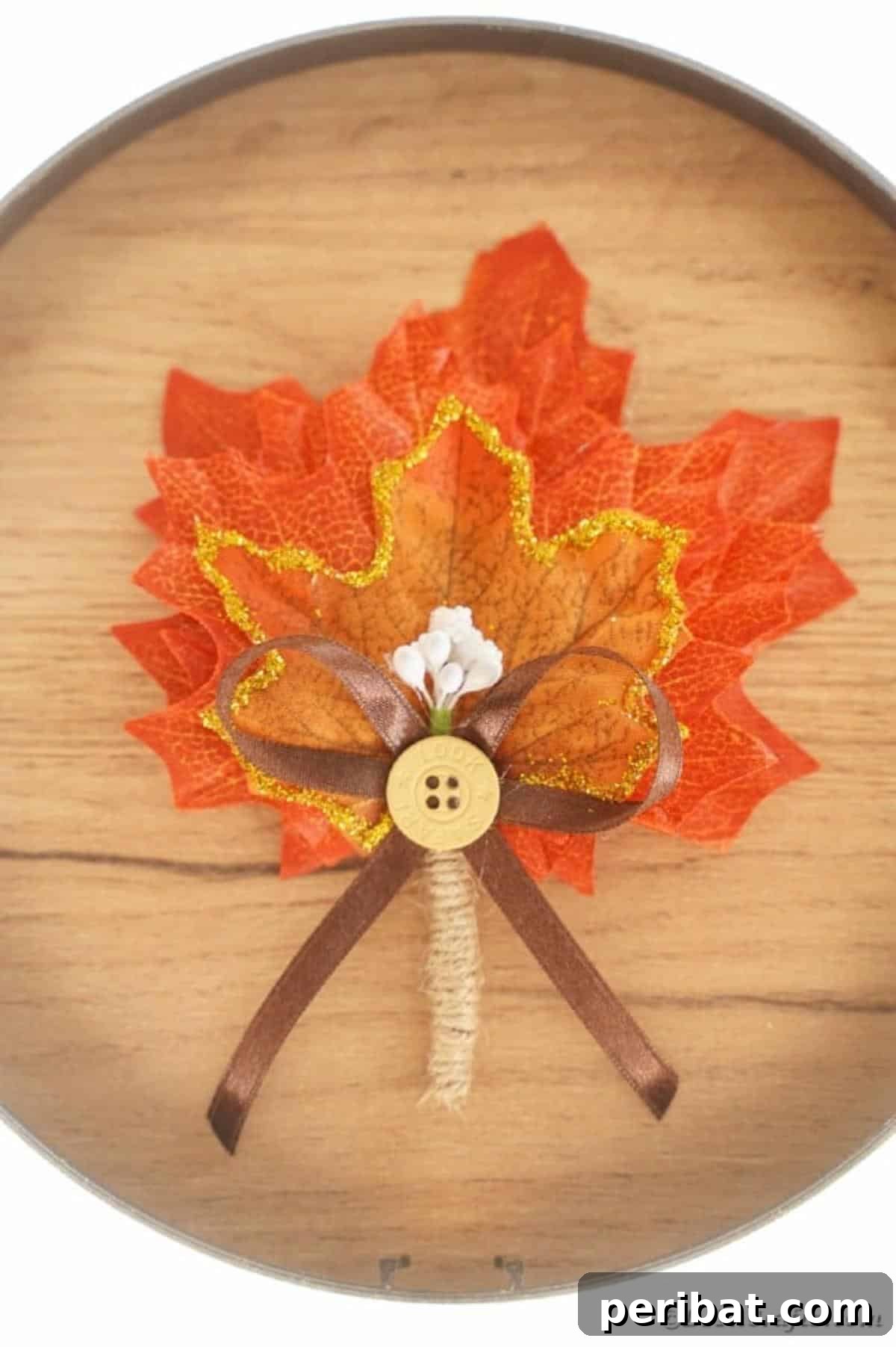 Elegant Autumnal Foliage Wedding Boutonnière 4 A close-up view of a fall leaf boutonniere resting on a rough wooden surface, highlighting the detailed texture of the leaves, the twine wrap, and the small button accent.