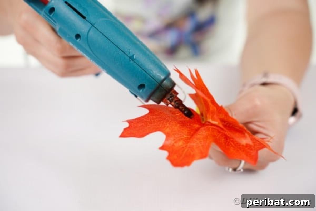 Elegant Autumnal Foliage Wedding Boutonnière 9 Hot glue being precisely applied to the edge of a single artificial leaf, preparing it for glitter application.
