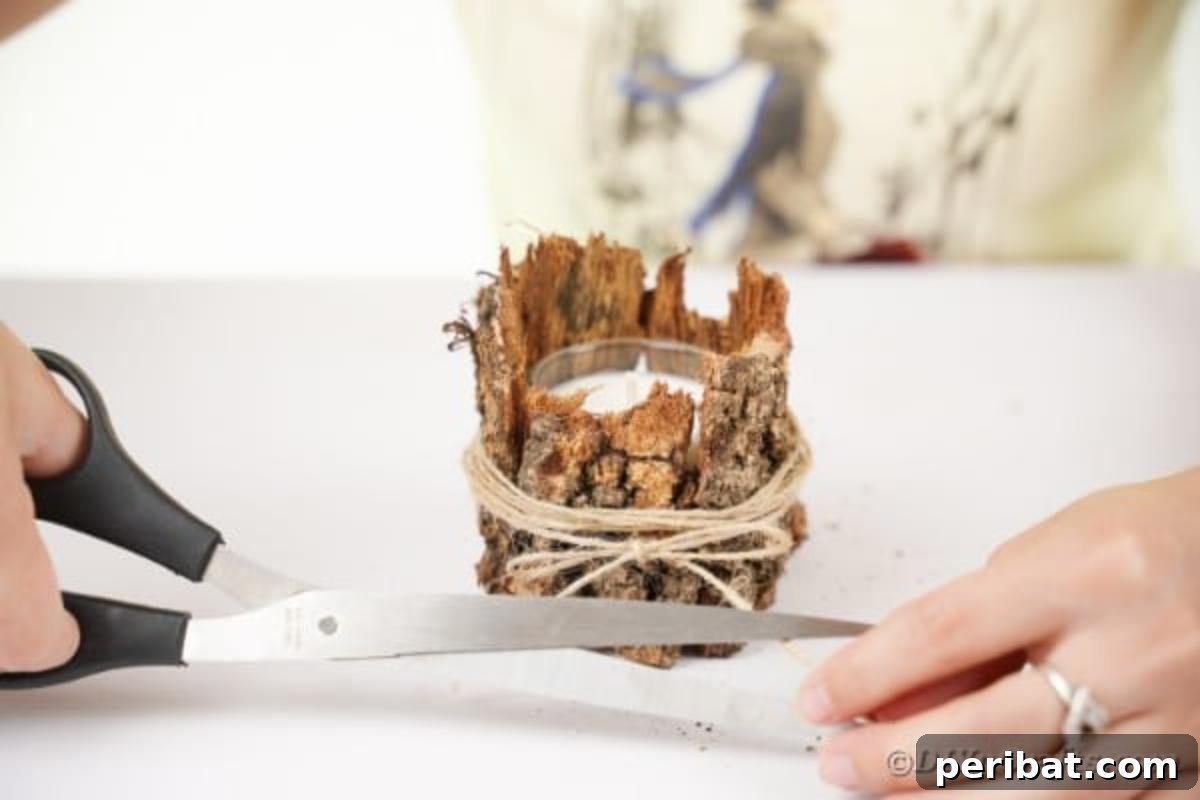 Woodland Hearth Bark Lantern 14 Scissors cutting excess twine after securing the bark around a candle holder, finishing the design