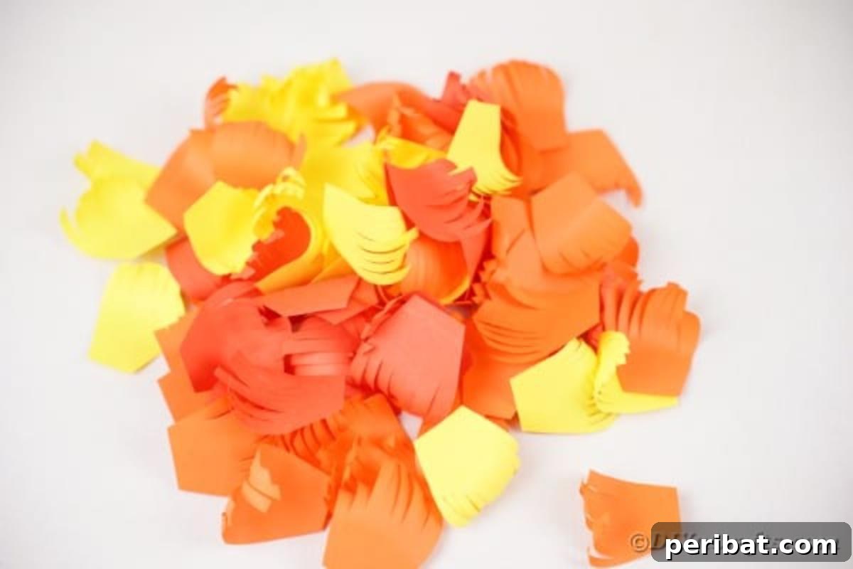 A stack of beautifully curled and fringed paper feathers in yellow, orange, and red, ready for assembly.