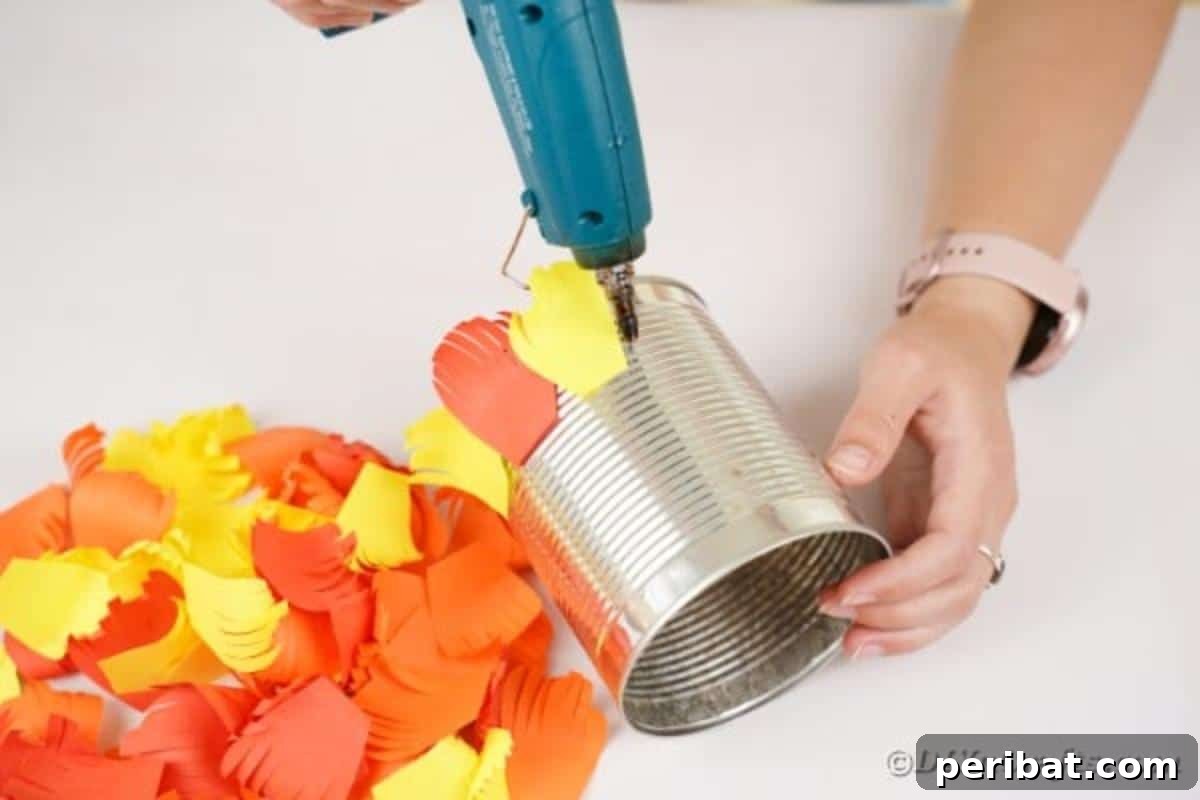 A close-up view of paper feathers being carefully glued onto the bottom of a tin can, showing the layering process.