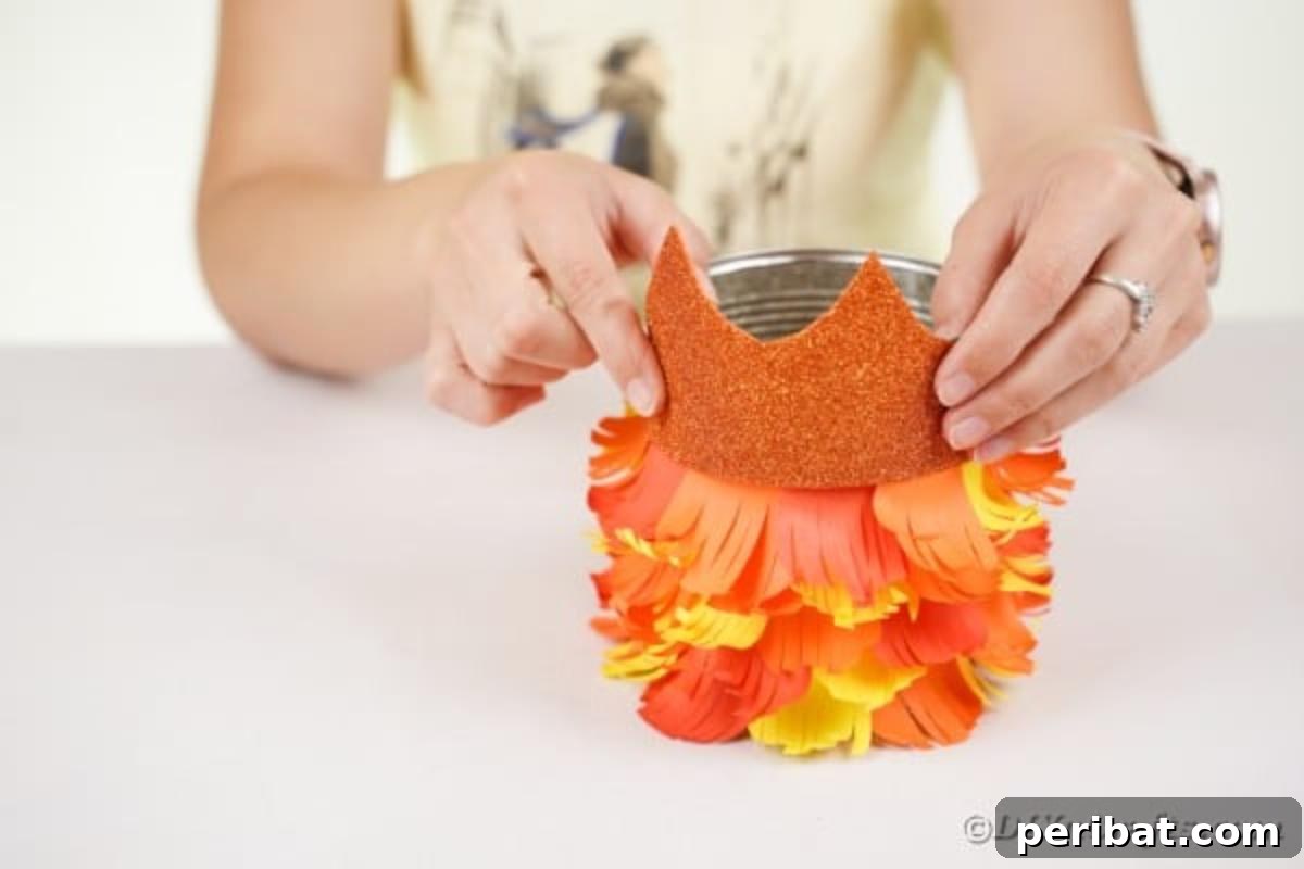 The glitter paper owl face being glued onto the top part of the tin can, completing the head section.