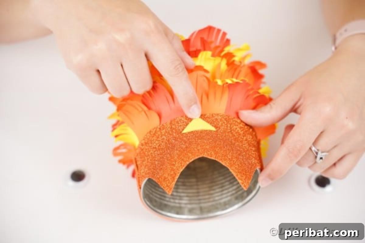 A small yellow paper triangle being glued onto the glitter paper owl face, forming the owl's beak.