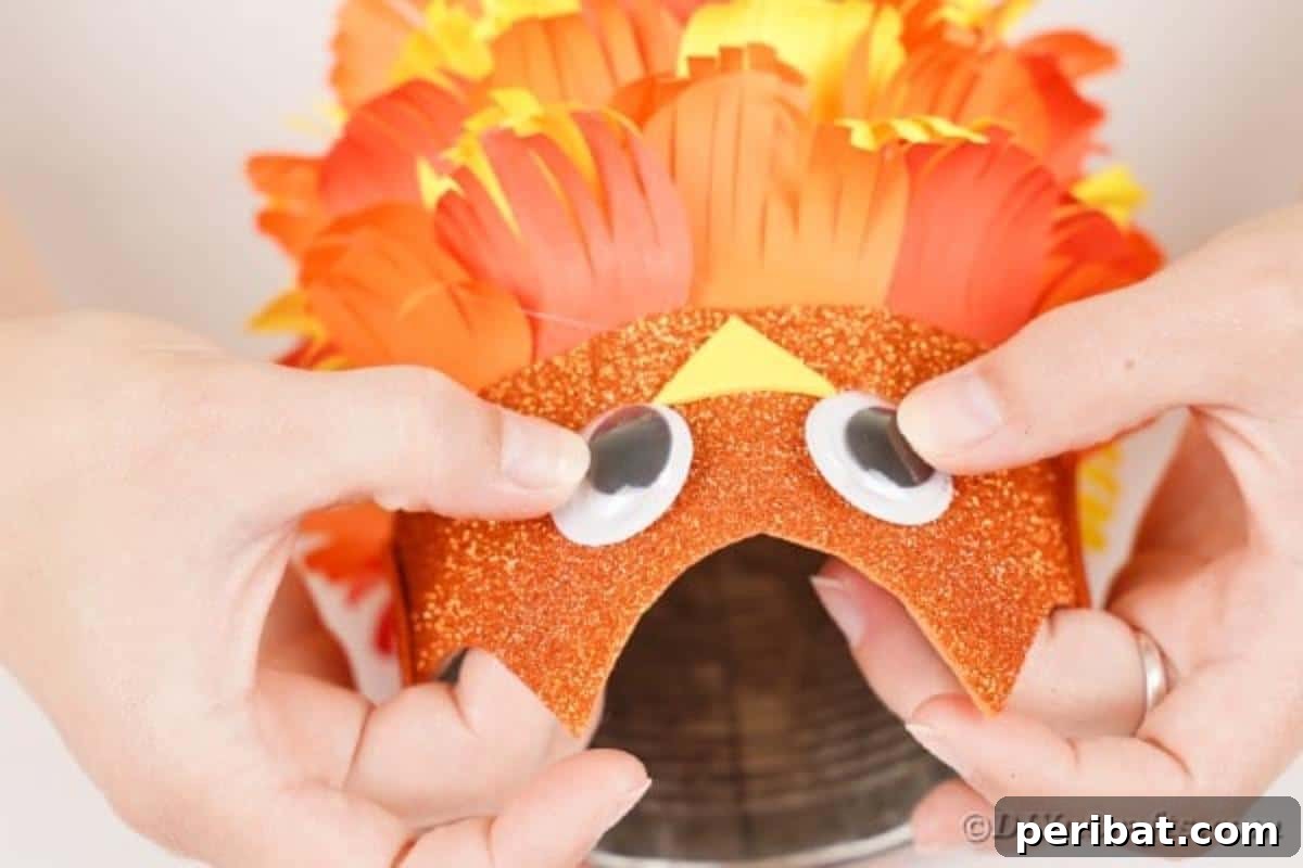Two googly eyes being affixed to the glitter paper owl face, bringing the owl's expression to life.