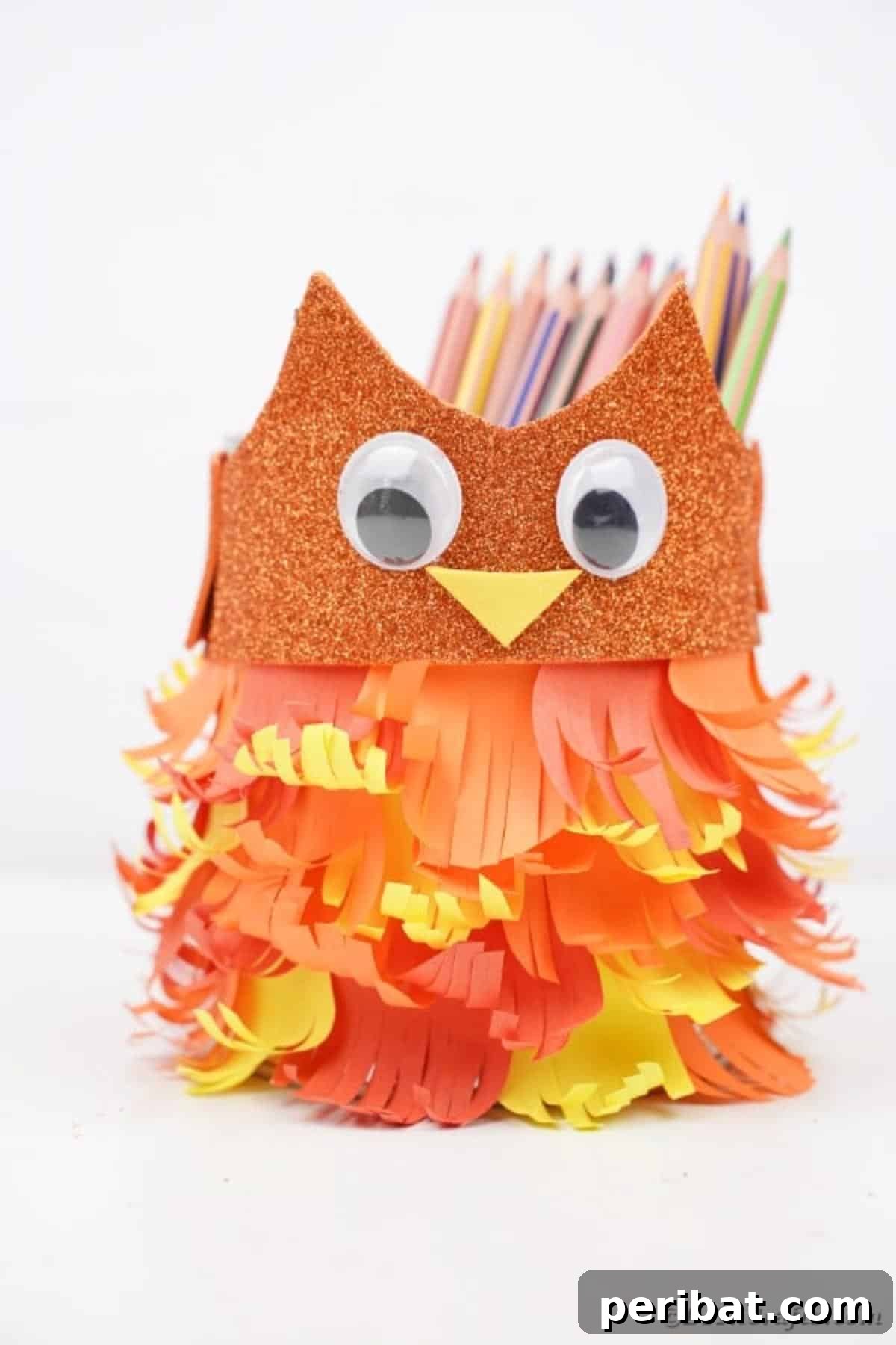 An upcycled tin can owl with vibrant, non-fall-themed paper feathers, displayed on a clean white counter.