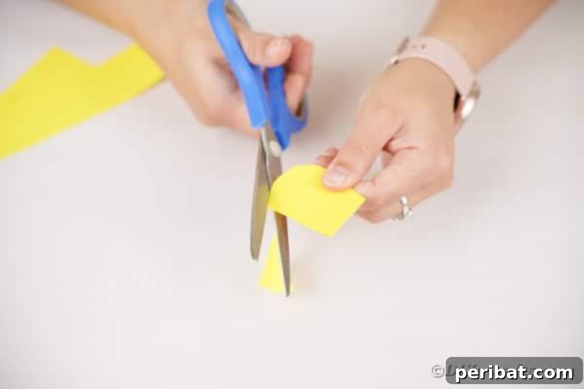 A hand cutting rounded shapes from folded craft paper, preparing them to be individual feathers.