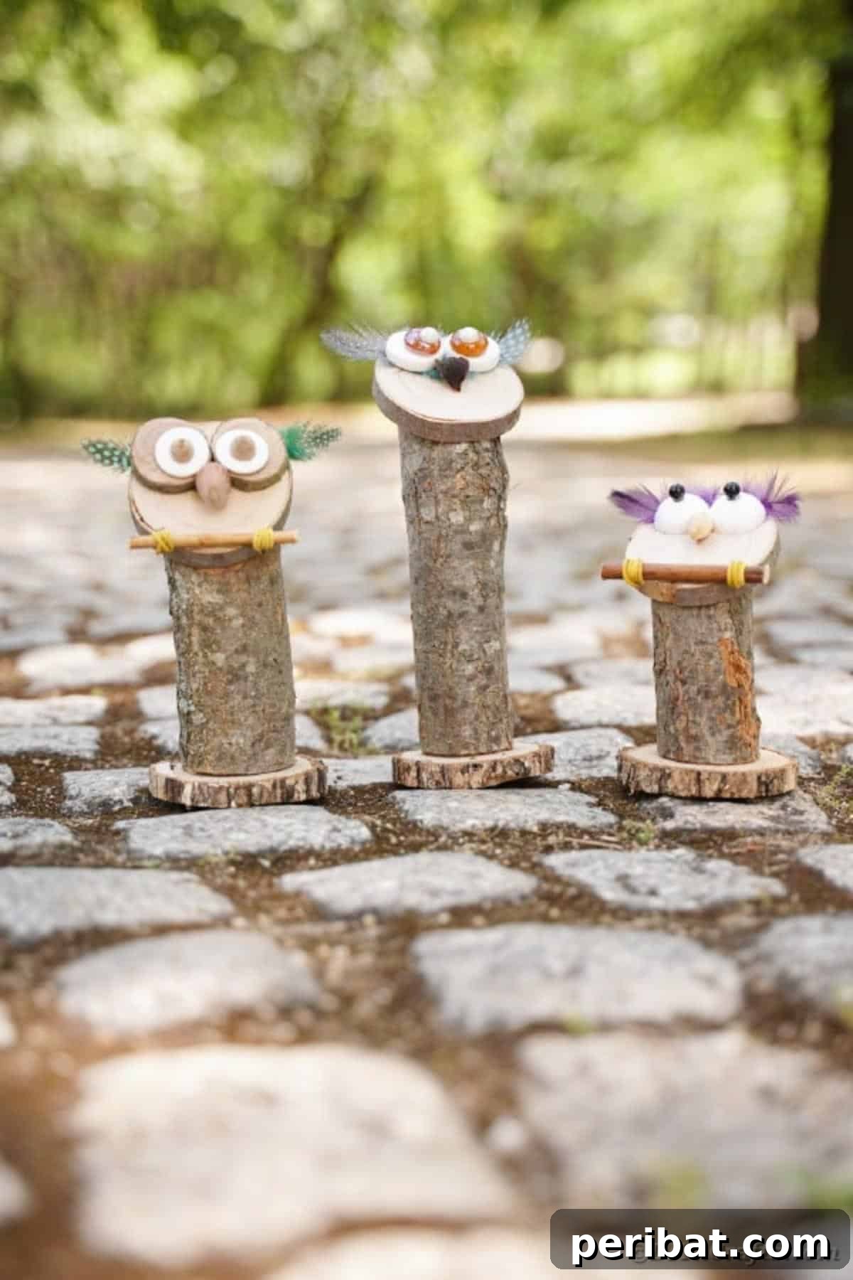 Whimsical Wooden Owls from Recycled Scraps Video Guide 18 An artistic ensemble of three uniquely decorated wooden owls, presented on a textured cobblestone surface, with one owl featuring bold, vibrant feathers around its eyes.