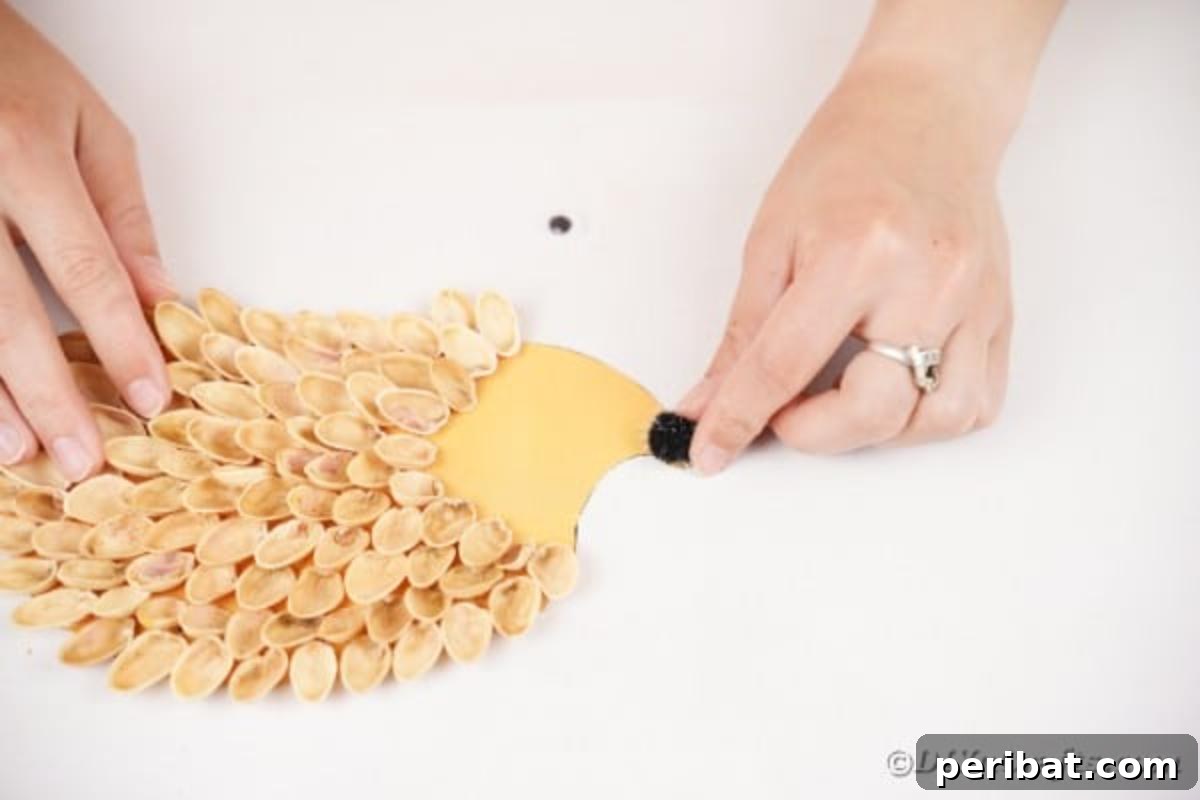 A hand gluing a small black pom pom onto the tip of the hedgehog's face to create its nose.