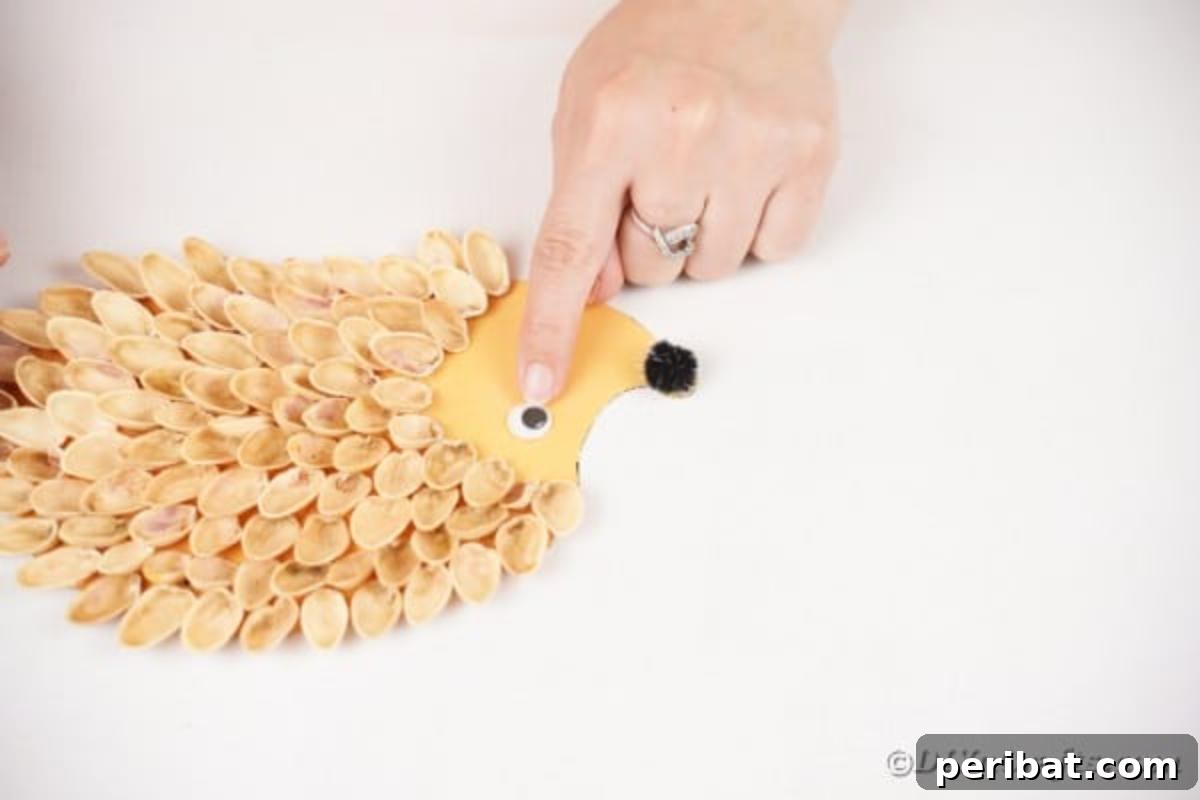 A googly eye being glued onto the face of the pistachio shell hedgehog.