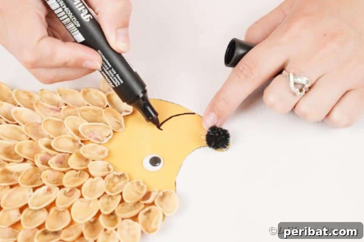 A black marker drawing a small smile onto the face of the pistachio shell hedgehog.
