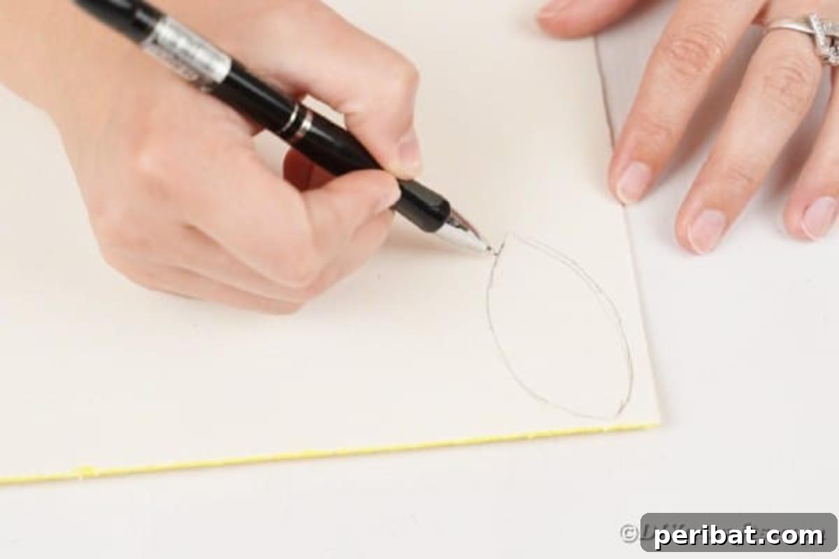A hand tracing a leaf shape onto the back of a yellow foam paper sheet.
