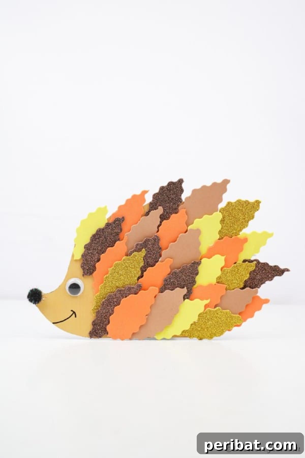 A finished paper leaf hedgehog craft, richly textured with colorful foam leaves, displayed on a clean white table.