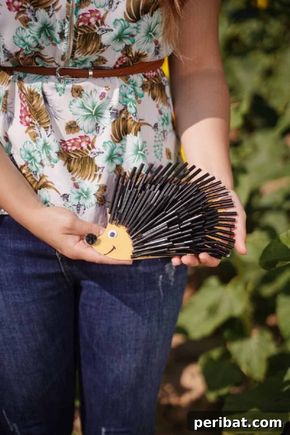 A woman holding a finished hedgehog craft made with black straws, showcasing its texture and ready for display.
