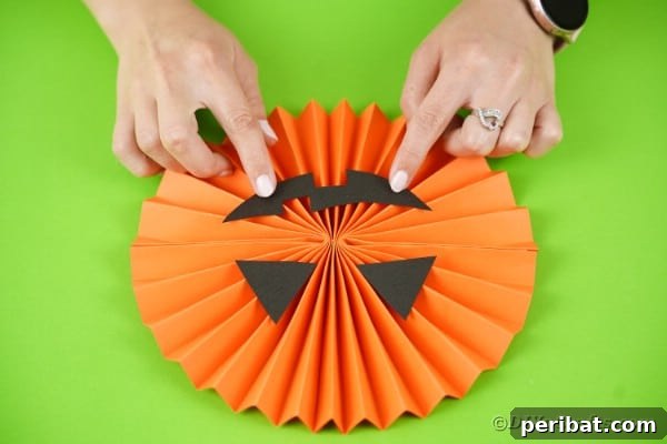 Fun and Easy Halloween Paper Fan Decor 37 Gluing mouth onto pumpkin paper fan