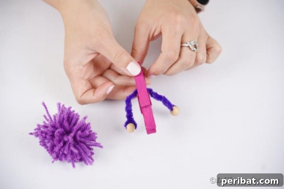 Spooktacular Clothespin Monster Craft 15 A person gluing a pipe cleaner arm onto a painted clothespin