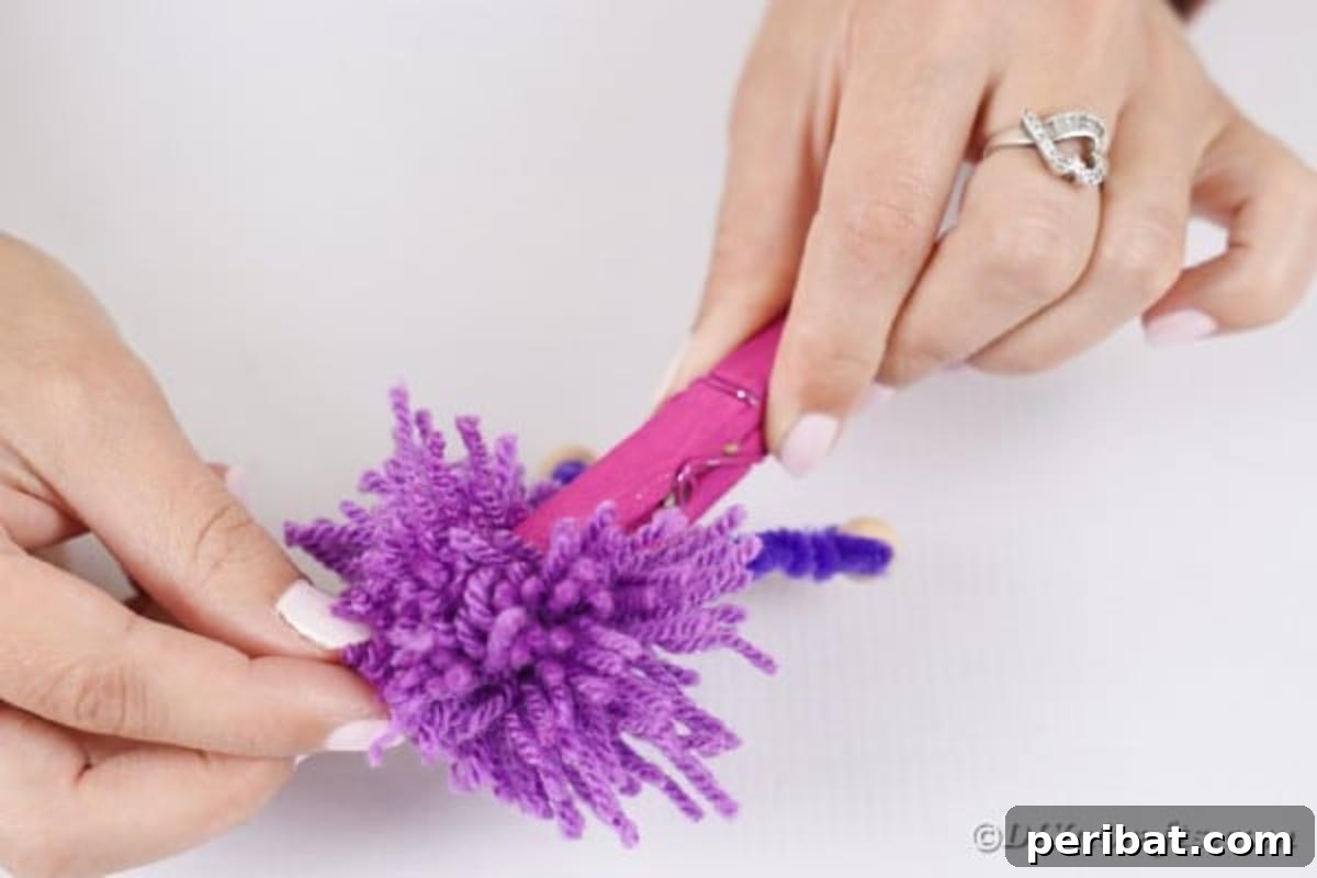 Spooktacular Clothespin Monster Craft 16 A person gluing a yarn pom-pom onto the top of a clothespin, creating hair for the monster