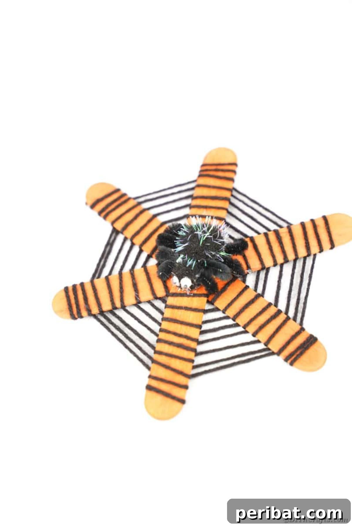 Spooky Stick Spiderwebs 18 A finished craft stick spider web, complete with its friendly pom-pom spider, displayed beautifully on a white table.