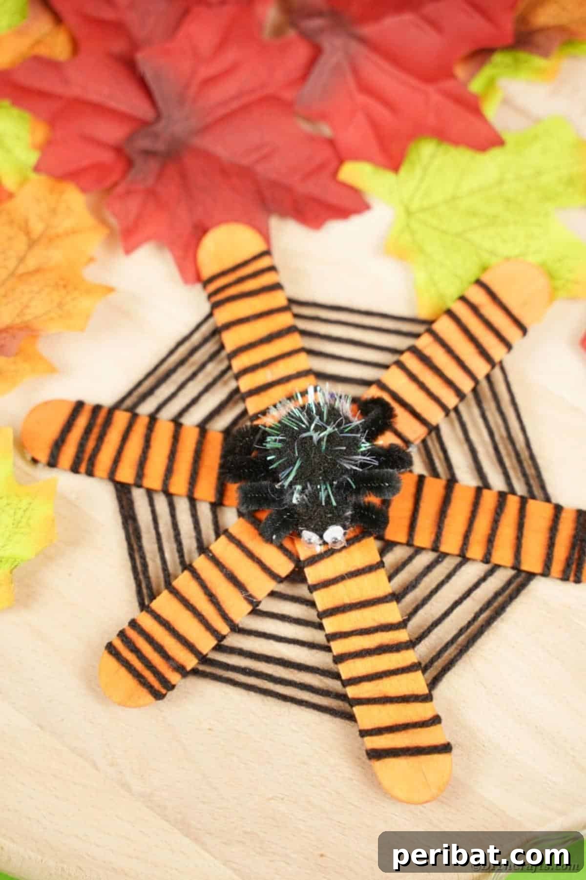 Spooky Stick Spiderwebs 21 A close-up of a craft stick spider web, featuring a sparkling pom-pom spider, set against a backdrop of fall leaves.