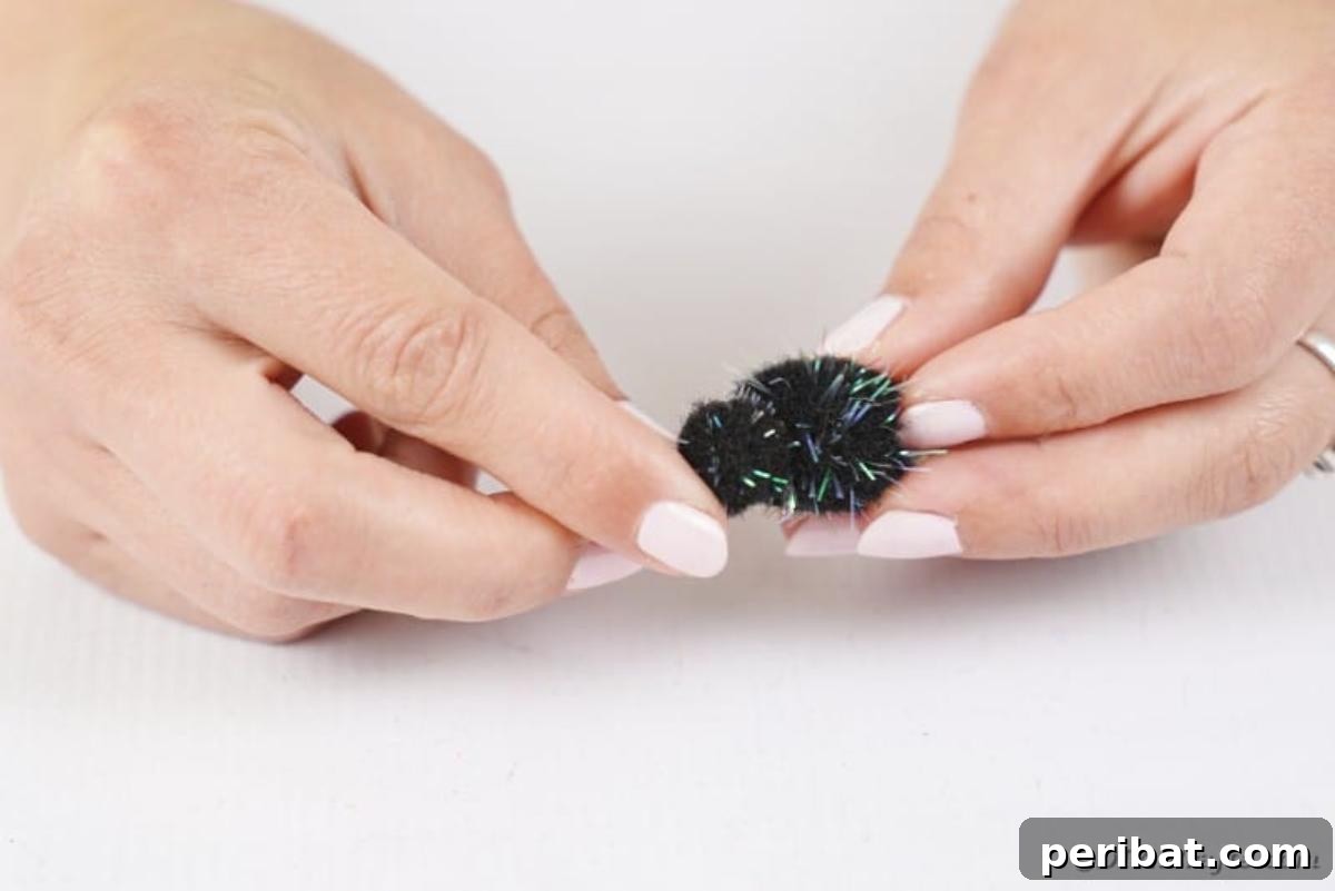 Spooky Stick Spiderwebs 9 A pair of small black pom-poms, one medium and one small, are being glued together to form the spider's body and head.