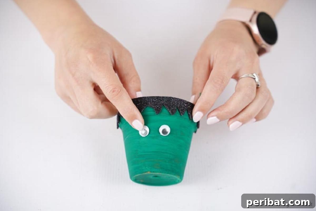 Charming Upcycled Planter Halloween Pals 18 Attaching googly eyes to the green flower pot, just below Frankenstein's hair.
