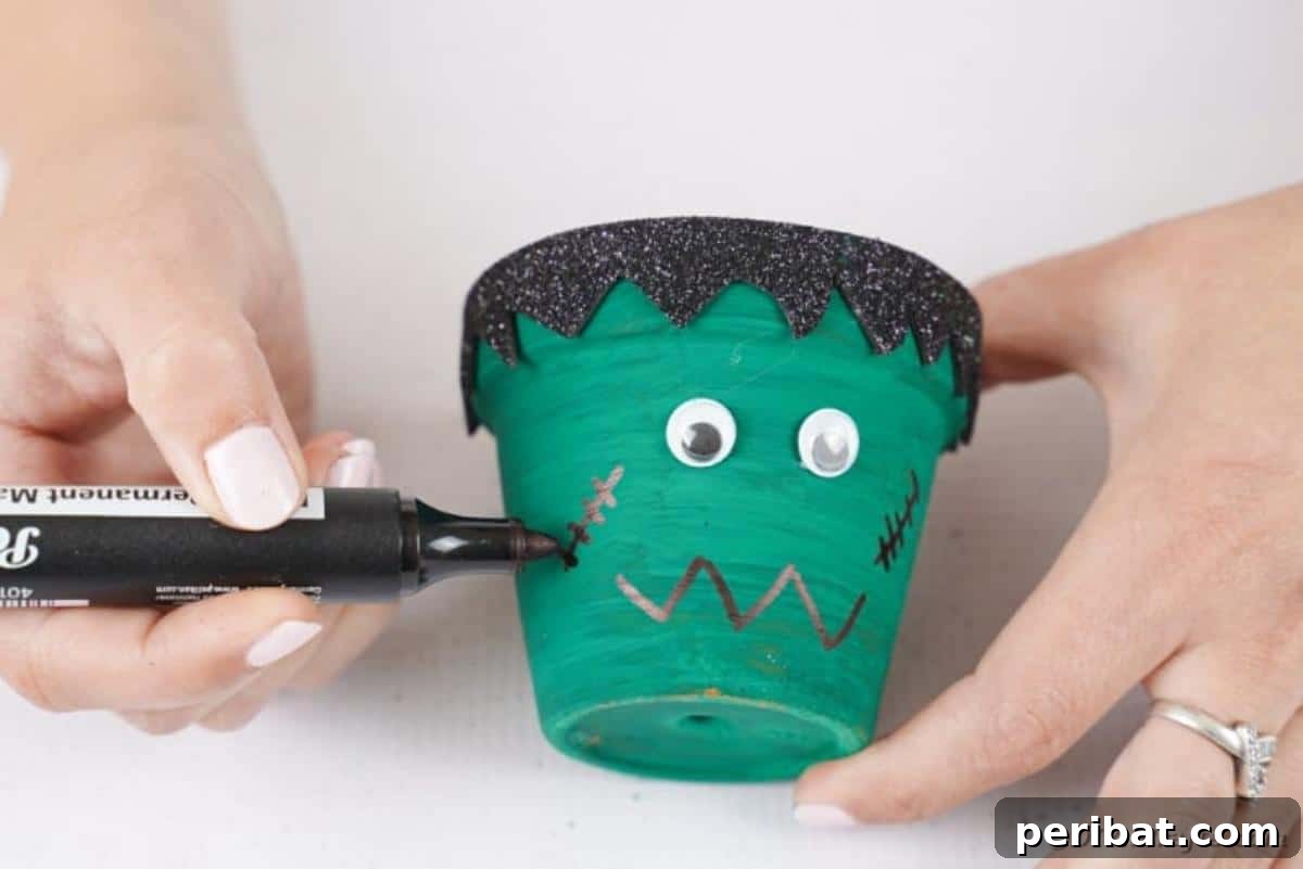 Charming Upcycled Planter Halloween Pals 19 Using a black paint pen to draw a jagged mouth and stitches on the Frankenstein flower pot.