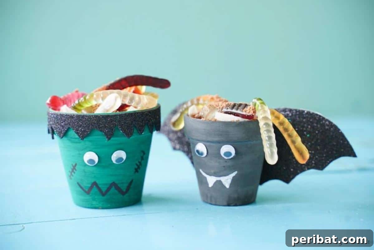 Charming Upcycled Planter Halloween Pals 4 A trio of flower pot Halloween characters, including a bat and Frankenstein, filled with dirt dessert and candy on a blue table.