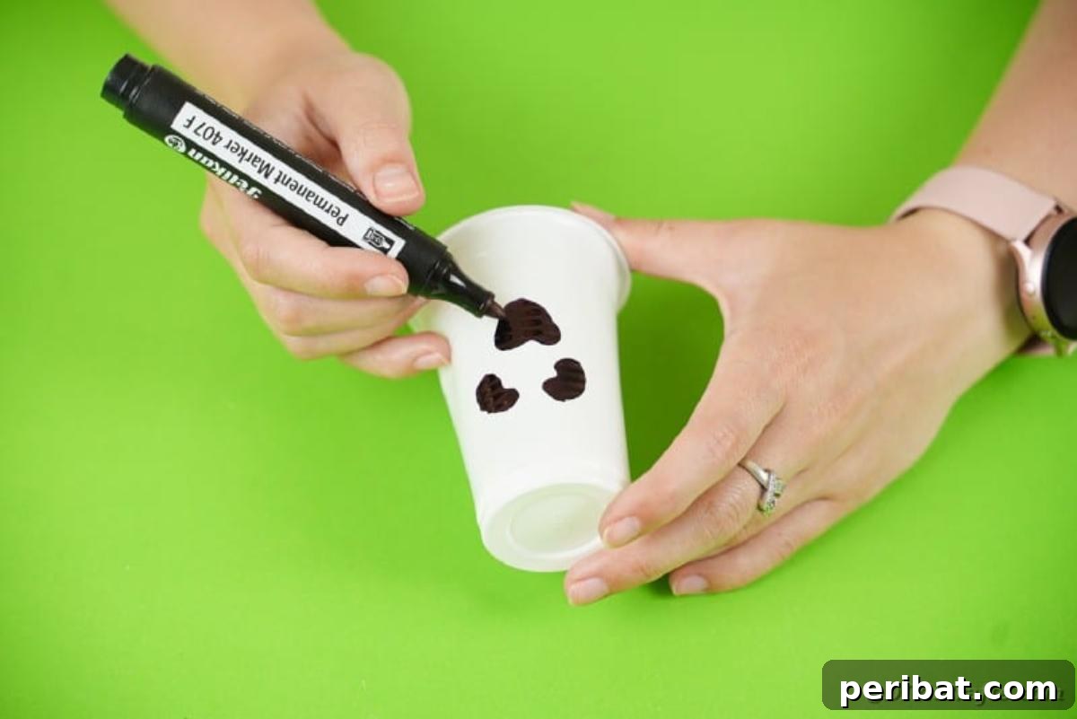 A hand drawing the simple, expressive face of a ghost onto a white plastic cup.