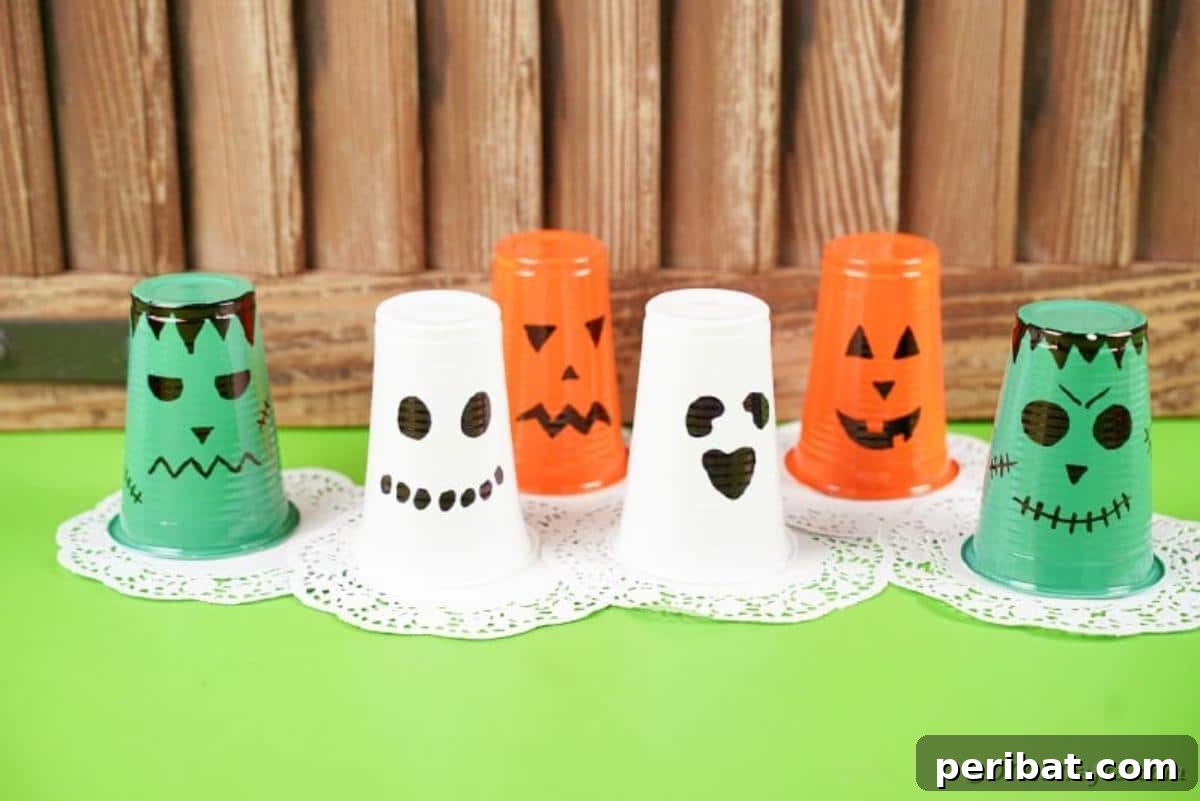 A trio of plastic cup lanterns, a ghost, pumpkin, and Frankenstein, neatly arranged on a green table.
